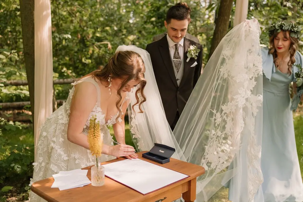 formalności do ślubu, jak zorganizować ślub w plenerze, para młoda składa podpisy na dokumentach